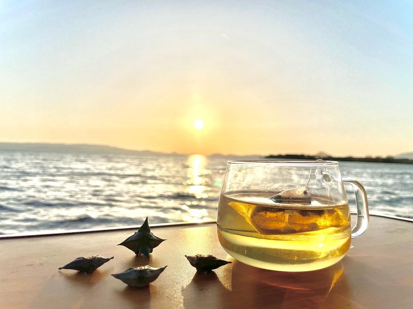 夕日の猪苗代湖を背に、ガラスのマグに入ったひし茶とヒシの実